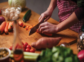 A person chopping carrots on a counter full of vegetables.